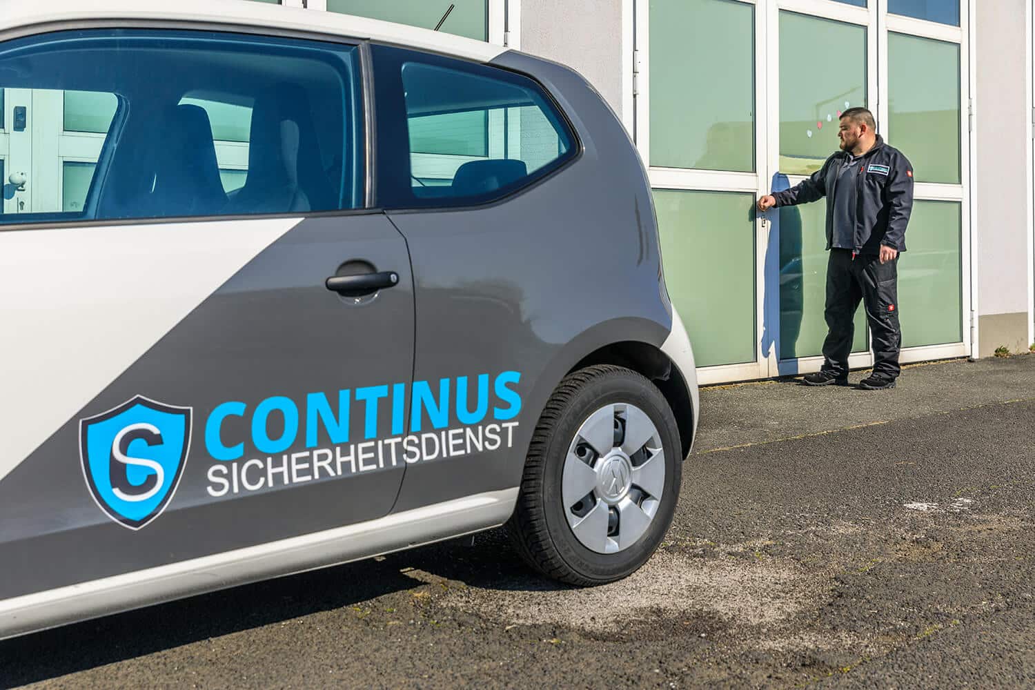 Graues foliertes Auto mit Continus Security Logo und Schriftzug. Im Hintergrund ein Mitarbeiter.